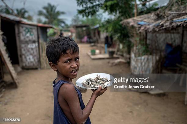 Young boy carrying plates of shrimp by one of the IDP camps, May 25, 2015 in Sittwe, Burma. Since 2012, the minority group of the Rohingya people are...