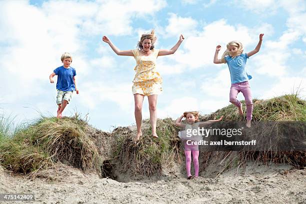 mother with three children jumping off dunes, wales, uk - axel jump stockfoto's en -beelden