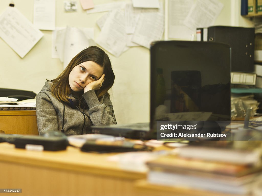Bored young woman at desk leaning on elbow