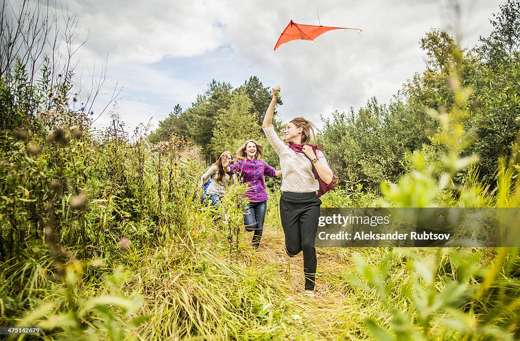 Four young women running through scrubland with kite