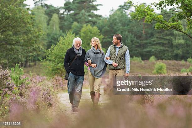 senior man, mid adult man and woman walking through forest - arm in arm stock pictures, royalty-free photos & images