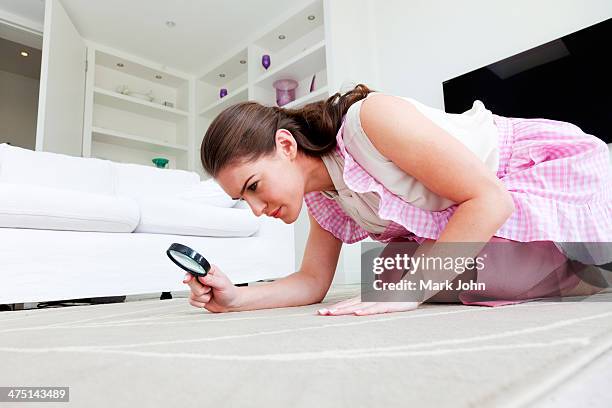 young woman on hands and knees inspecting rug with magnifying glass - obsessive stockfoto's en -beelden