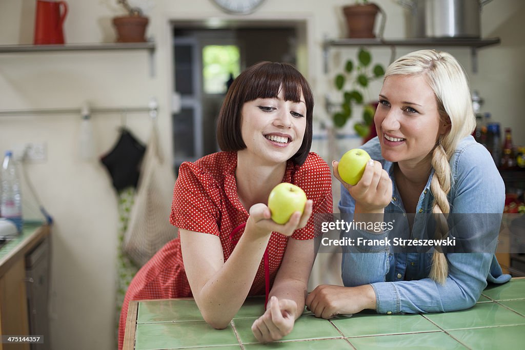 Two young women in kitchen holding apples