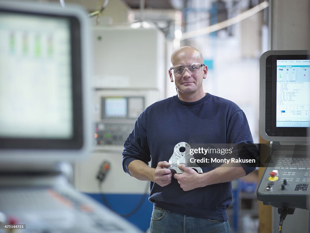 Engineer holding complex metal component in factory, portrait