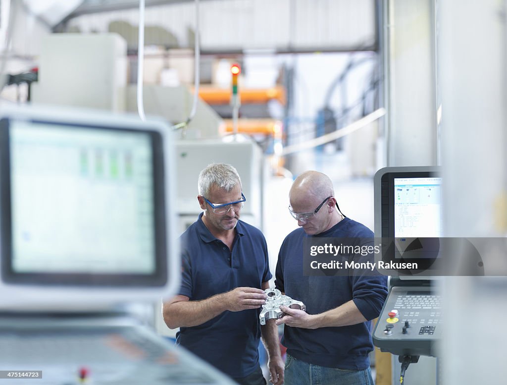 Engineers inspecting complex metal component in factory