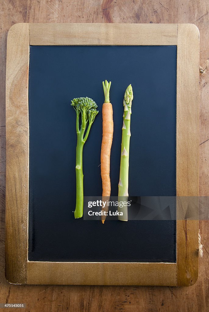 Carrot, broccoli and asparagus on blackboard, still life