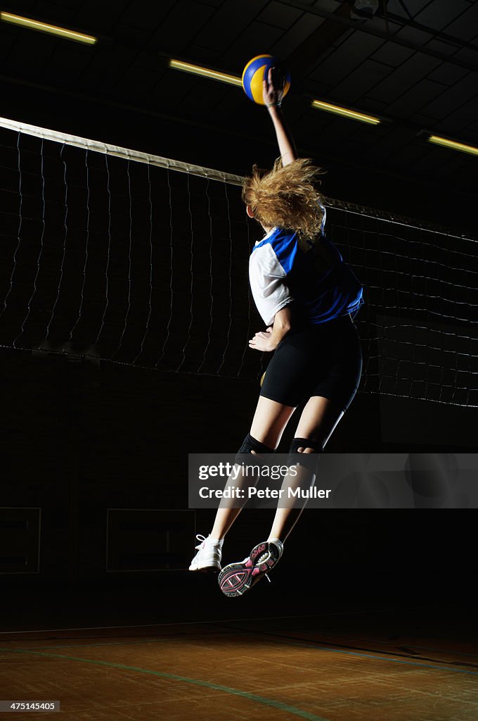 Volleyball player jumping for ball by net