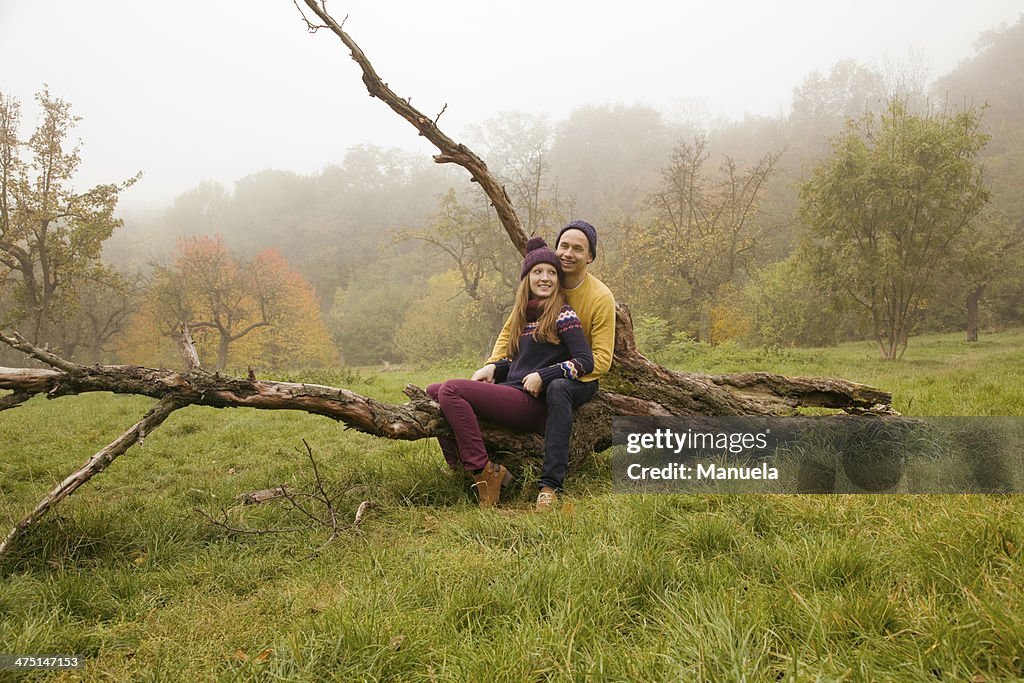 Young couple sitting on bare tree in misty park