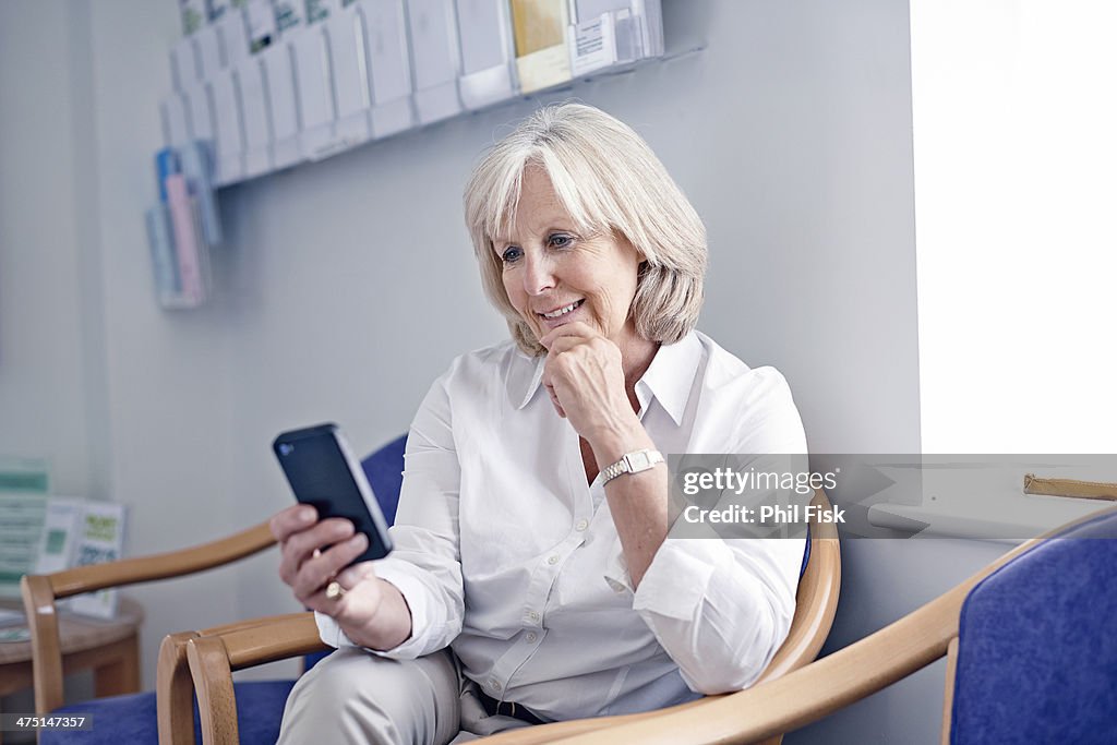 Mature female patient looking at mobile phone in hospital waiting room