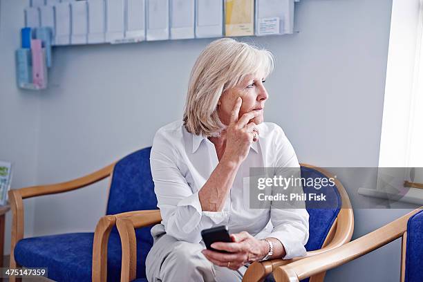 mature female patient with mobile phone in hospital waiting room - waiting room stock pictures, royalty-free photos & images