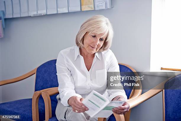 mature female patient reading leaflet in hospital waiting room - bulletin board flyer stock pictures, royalty-free photos & images