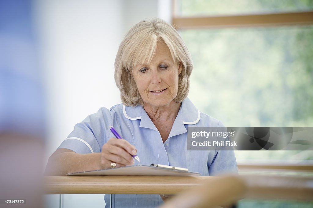 Mature female nurse in hospital corridor with clipboard