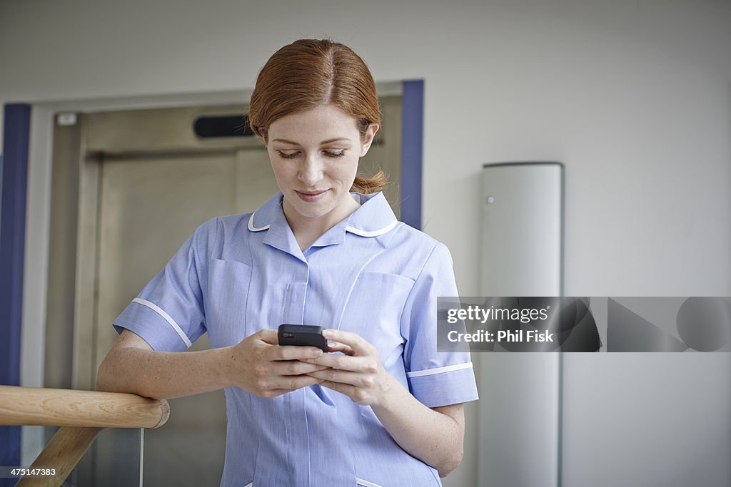 Female nurse looking at mobile phone outside hospital elevator