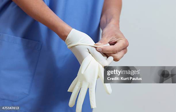 surgeon putting on latex gloves - operationskittel stock-fotos und bilder