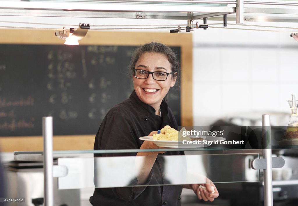 Woman working in restaurant kitchen, serving meal