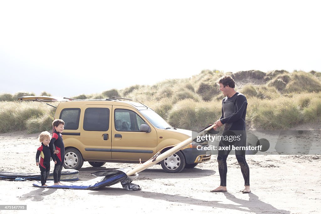 Father with two sons, surfboard and car on beach