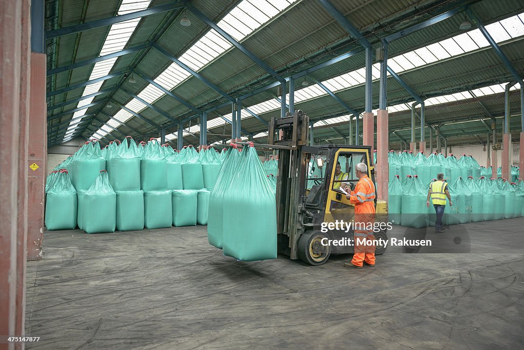 Workers and fork lift truck in bulk fertiliser store in port