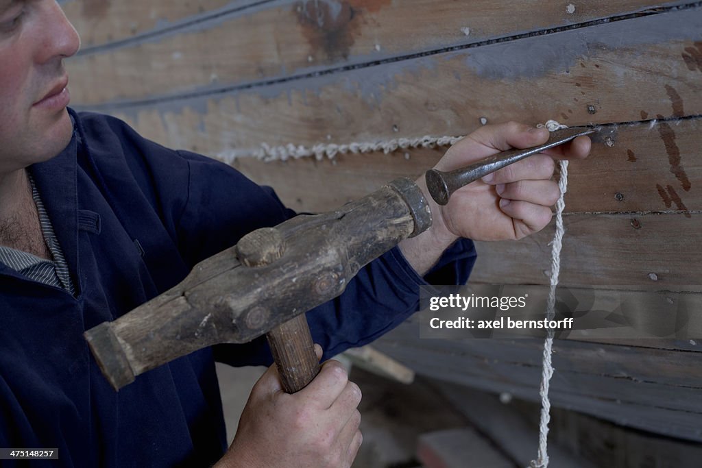 Man hammering string into boat  in workshop