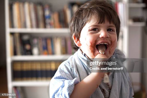portrait of male toddler licking chocolate covered teaspoon - chocolate face stock pictures, royalty-free photos & images