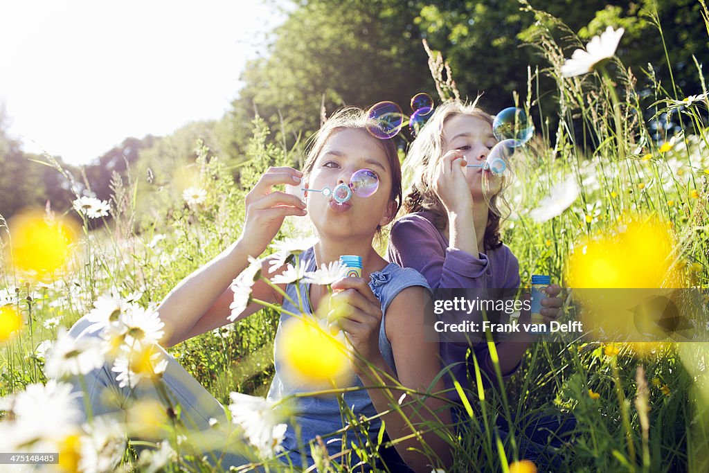 Sisters sitting in field of flower blowing bubbles