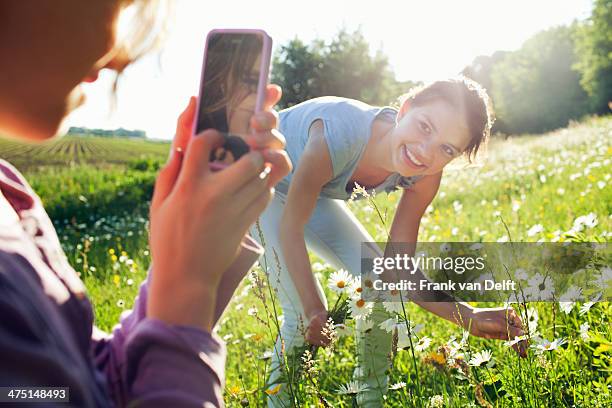 girl taking photograph of girl picking flowers - 12 12 12 2013 film stock-fotos und bilder