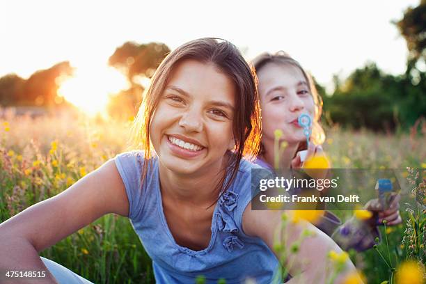 portrait of girls sitting in field, one blowing bubbles - schwester stock-fotos und bilder