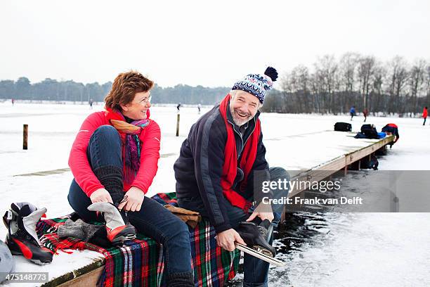 couple sitting on pier putting on ice skates - schaatsen stockfoto's en -beelden