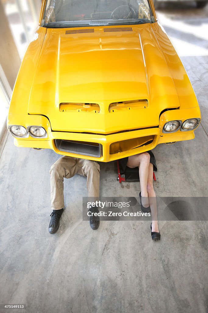 Man and woman lying underneath yellow vintage car