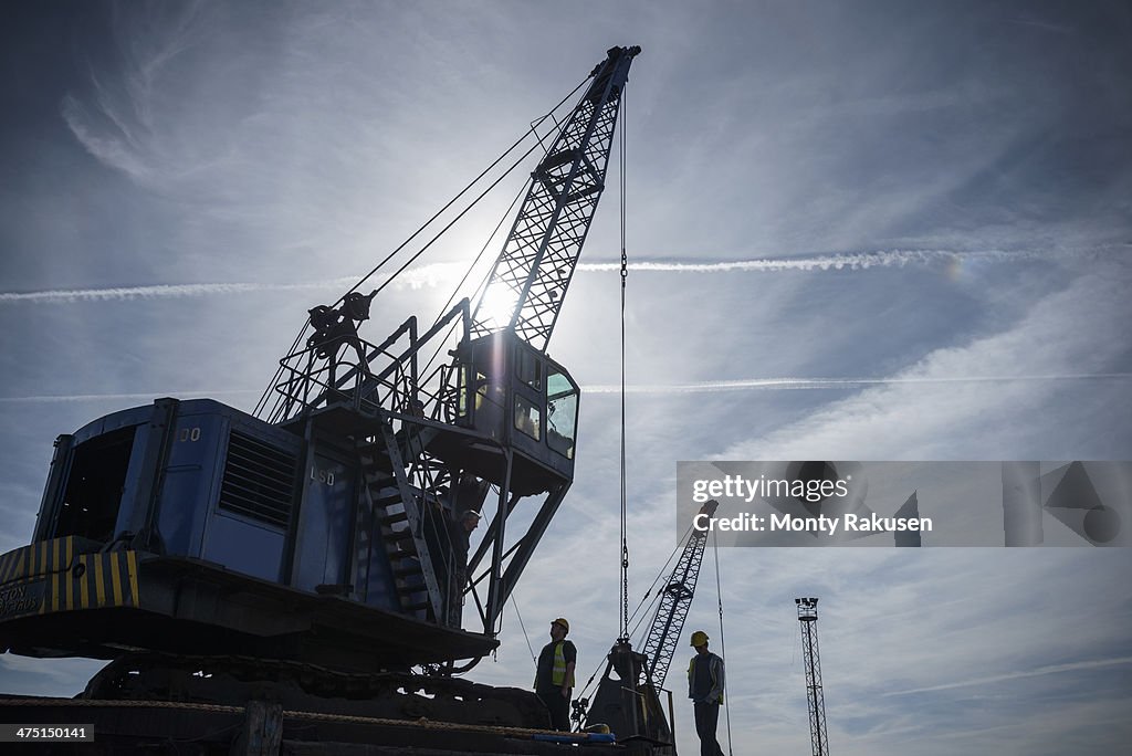 Low angle view of workers and crane in silhouette in port