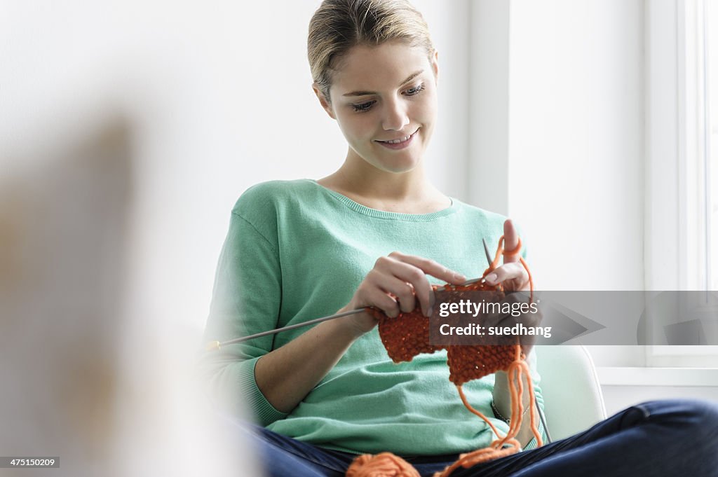 Young woman sitting in window seat knitting