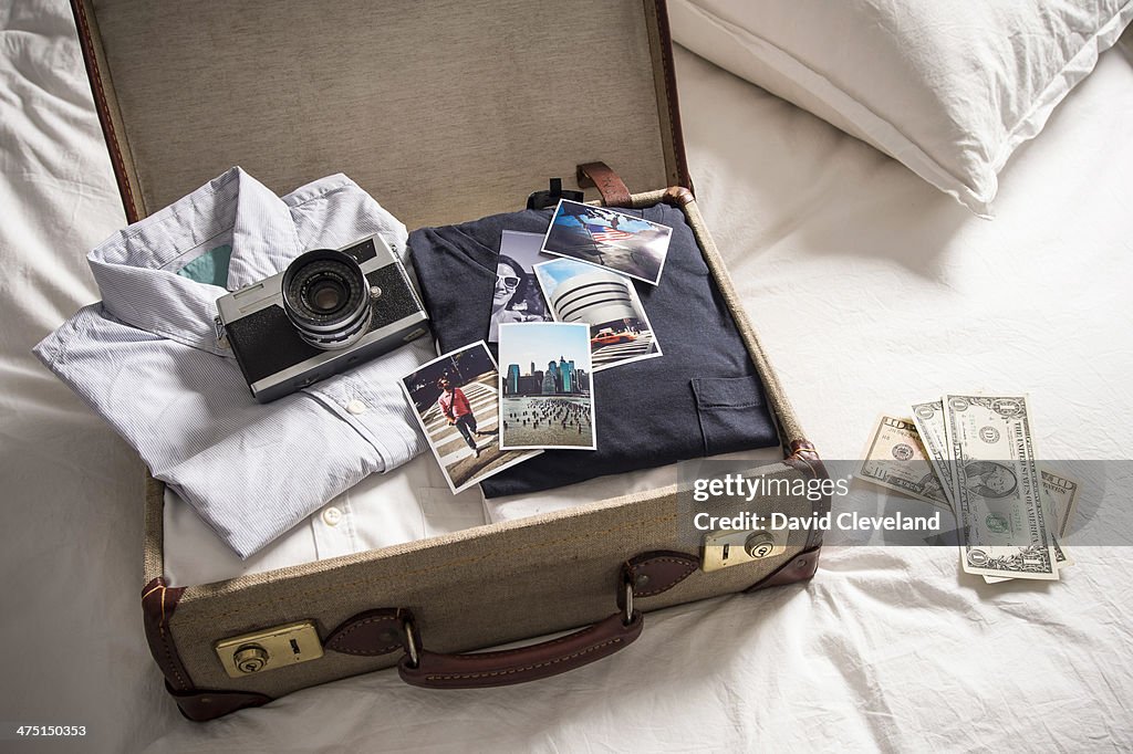 Open suitcase on bed with camera and photographs