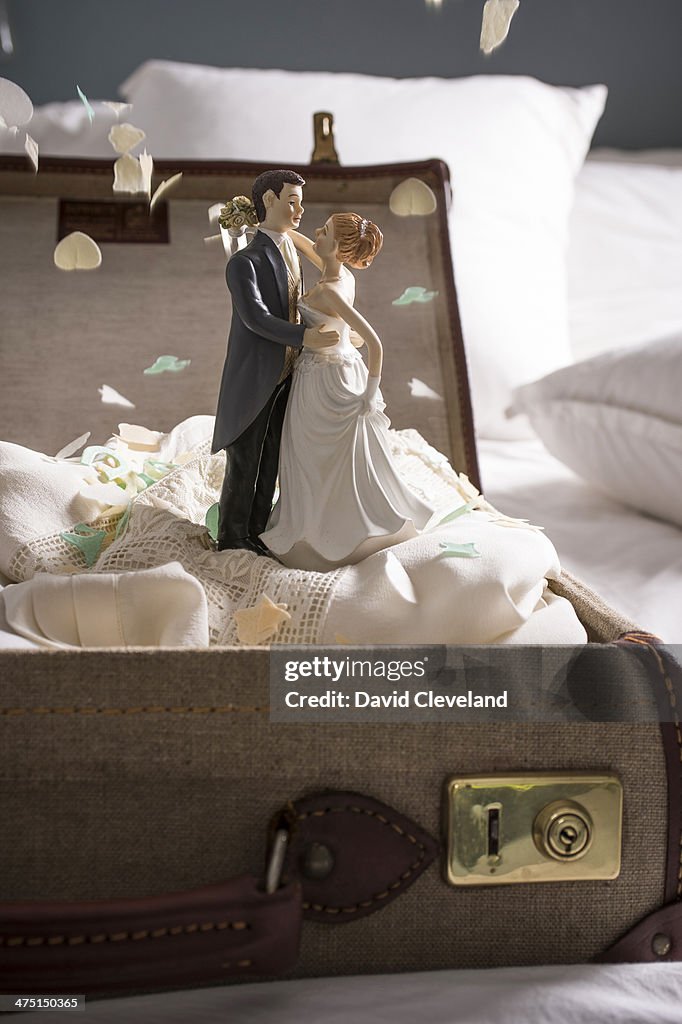 Open suitcase on bed with wedding figurines and confetti