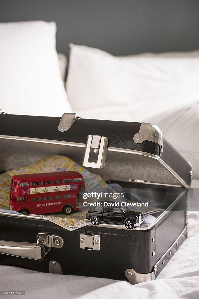 Open suitcase on bed with toy London bus and black cab