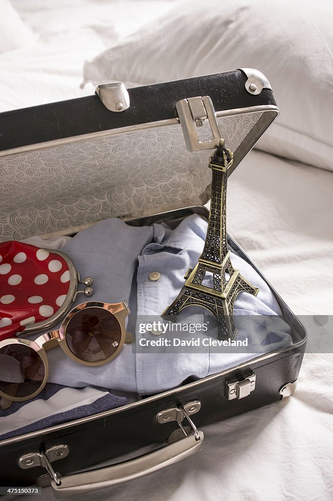 Open suitcase on bed with eiffel tower souvenir and sunglasses