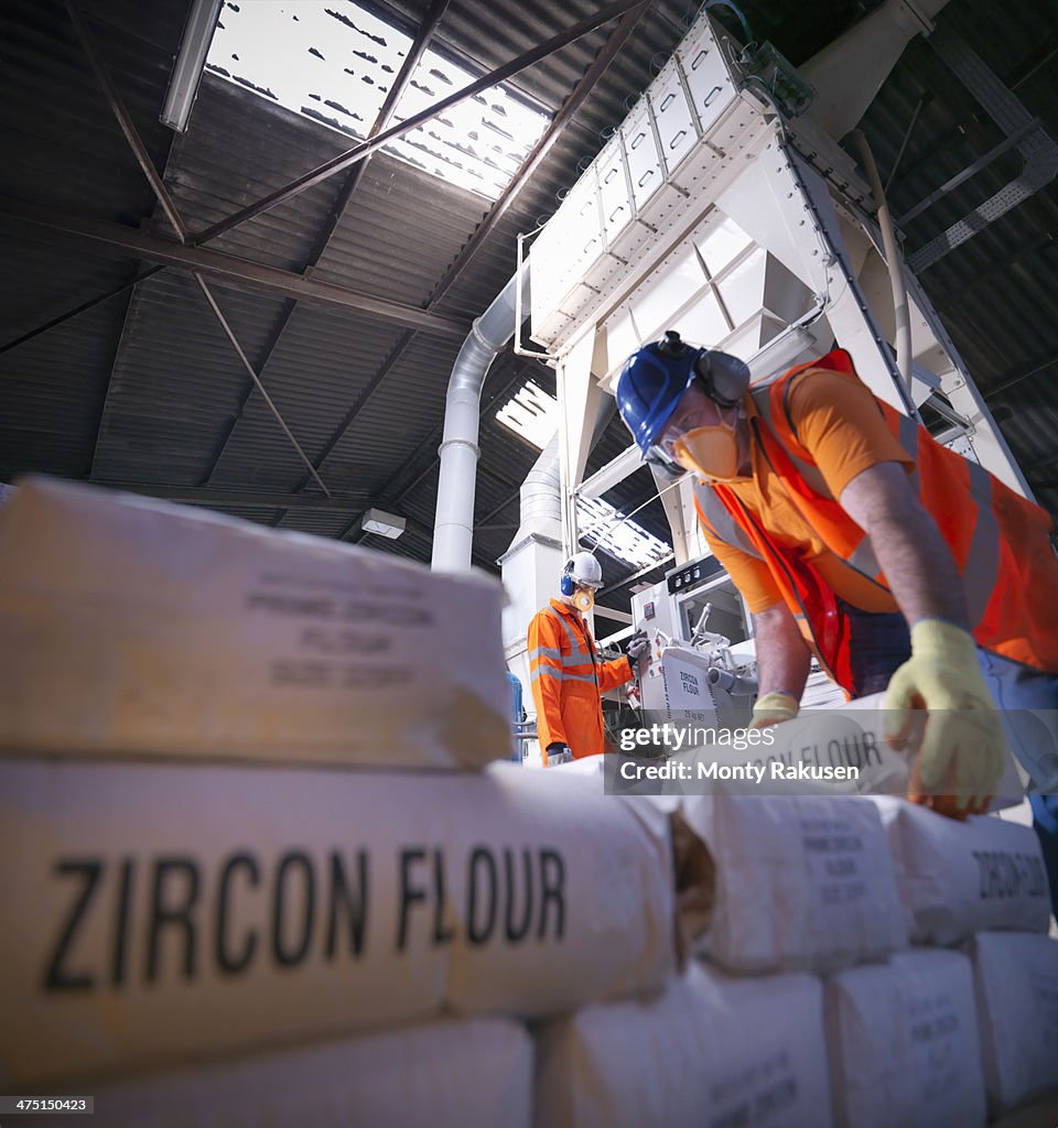 Workers in protective clothing filling zircon flour bags in mill, low angle view