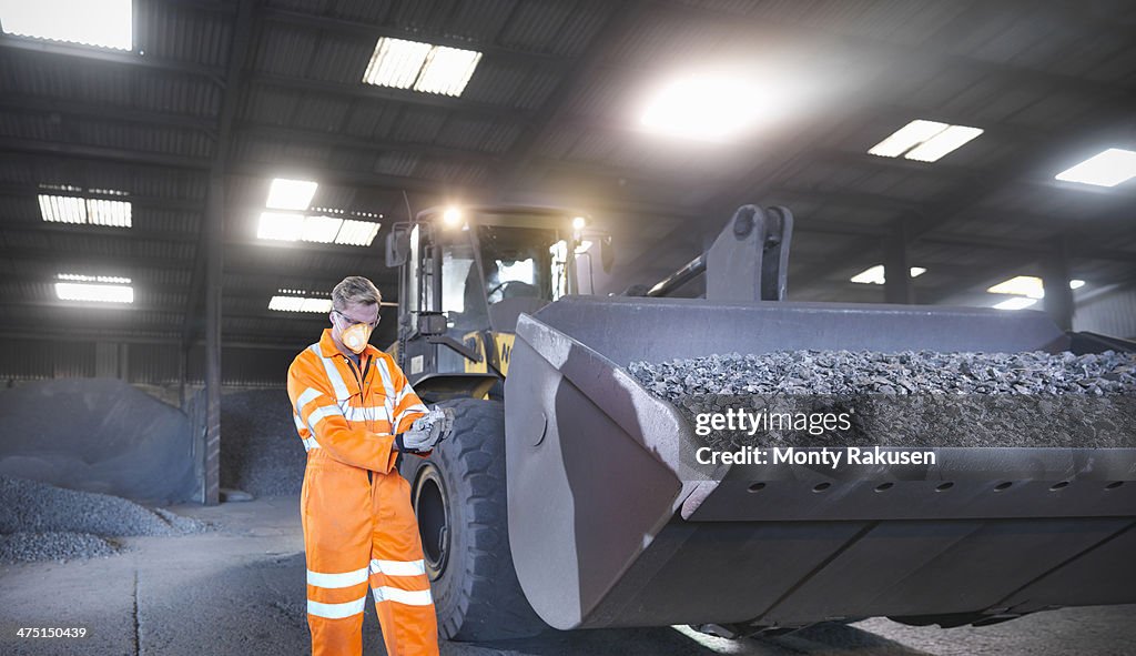 Worker in mineral store inspecting handful of metal alloy next to digger
