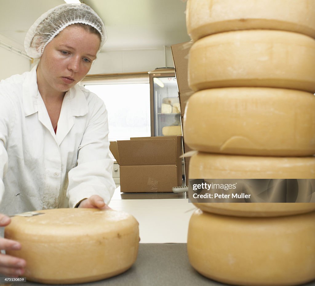 Worker with pile of cheese rounds at farm factory