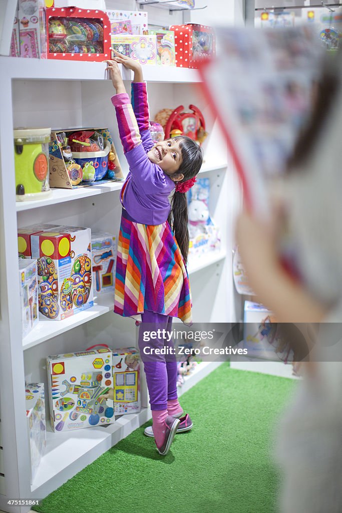 Young girl reaching up on tiptoe in toy shop