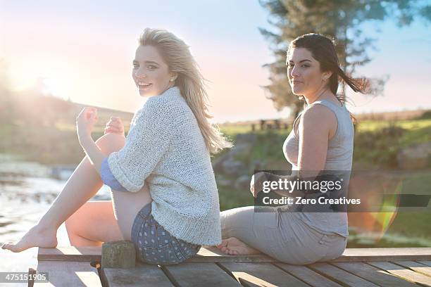 two female friends sitting on breezy pier - durbanville stock pictures, royalty-free photos & images