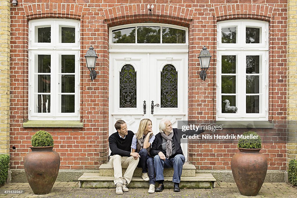Father and mid adult couple sitting on doorstep