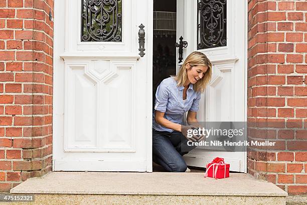 mid adult woman with gift on front doorstep - doorstep stock pictures, royalty-free photos & images