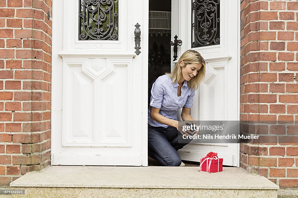 Mid adult woman with gift on front doorstep