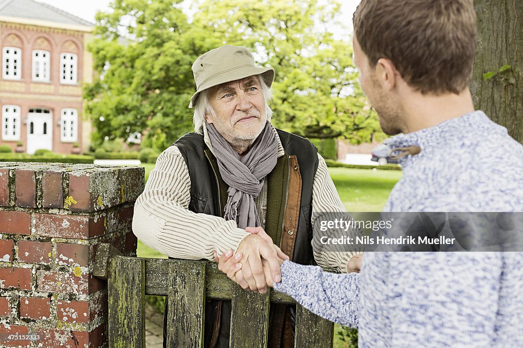 Senior man and mid adult man shaking hands over gate