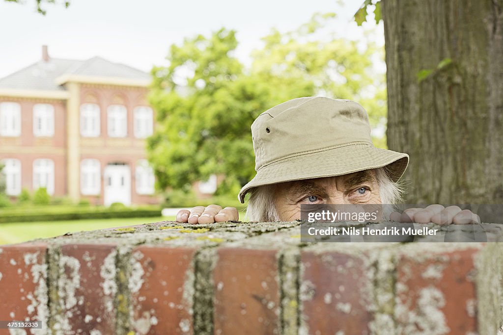 Senior man wearing hat peering over garden wall