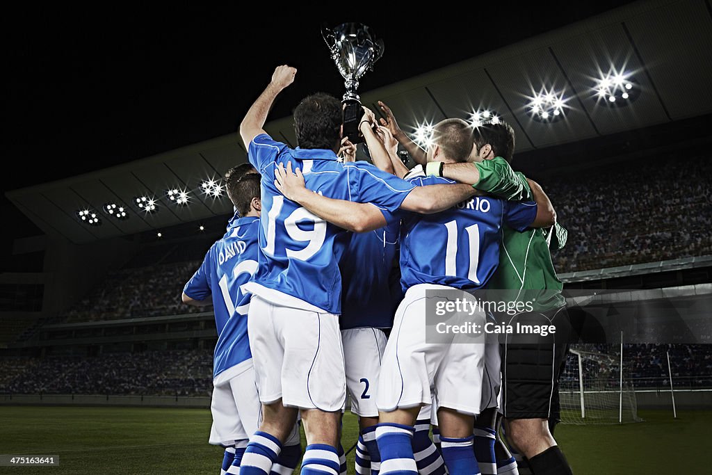 Soccer team cheering with trophy on field