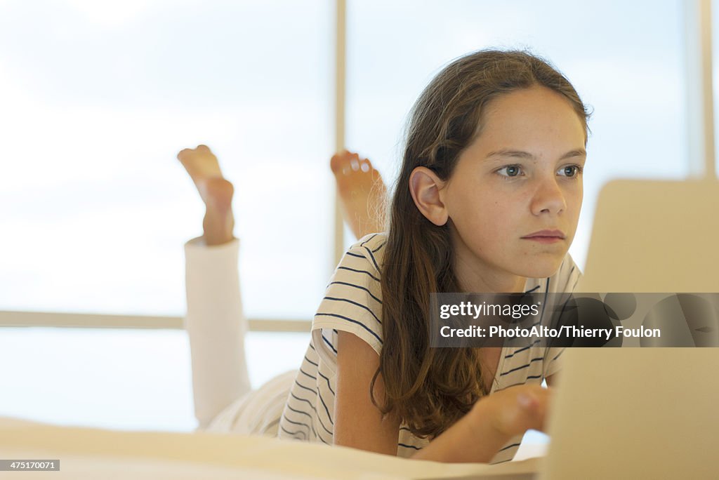 Preteen girl lying on stomach using laptop computer