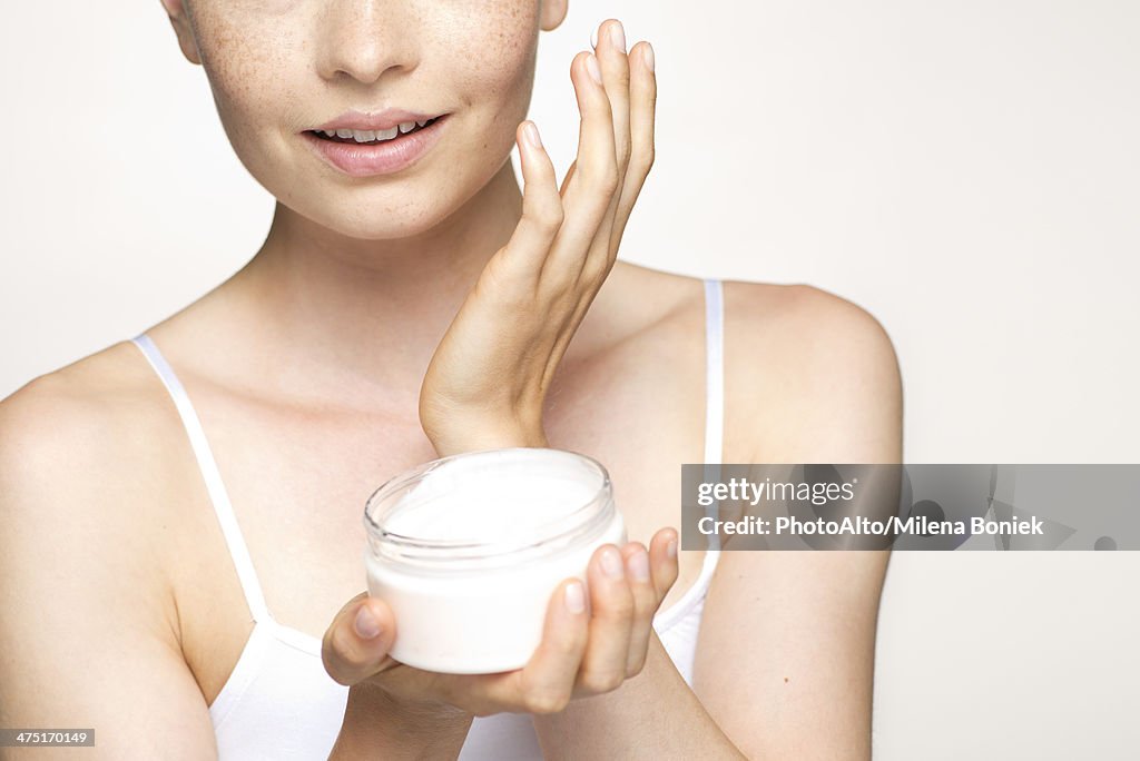 Young woman applying moisturizer to face, portrait