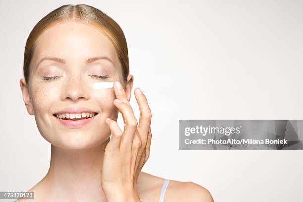 young woman applying mositurizer under eye - complexion foto e immagini stock