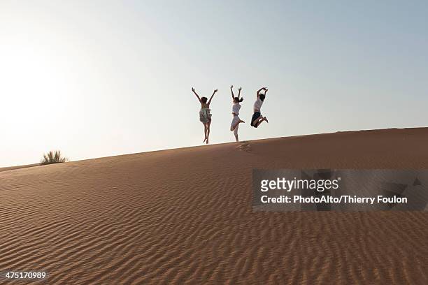children jumping on top of dune with arms raised in air - hot arabic girl stock pictures, royalty-free photos & images