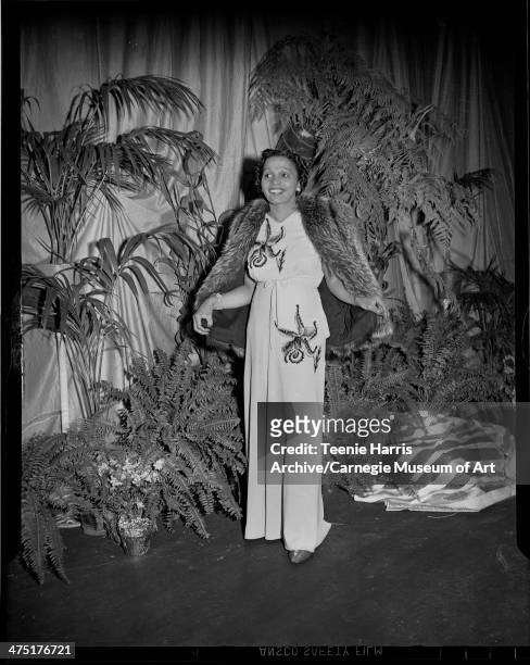 Hazel Betters modeling long gown with sequined floral design and fur jacket over shoulders, on stage with potted plants for sixth annual Beauty Shop...